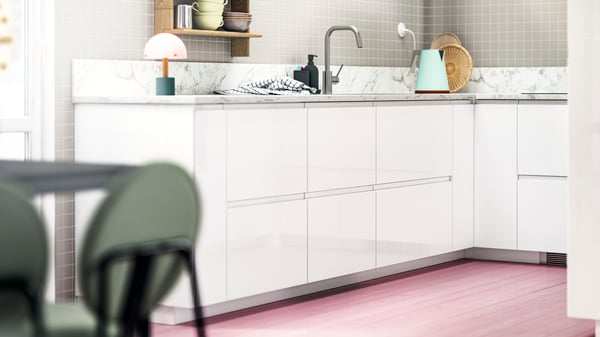 A modern kitchen with VOXTORP high-gloss white fronts, with pink floors, green chairs, and pops of colour on the shelves.