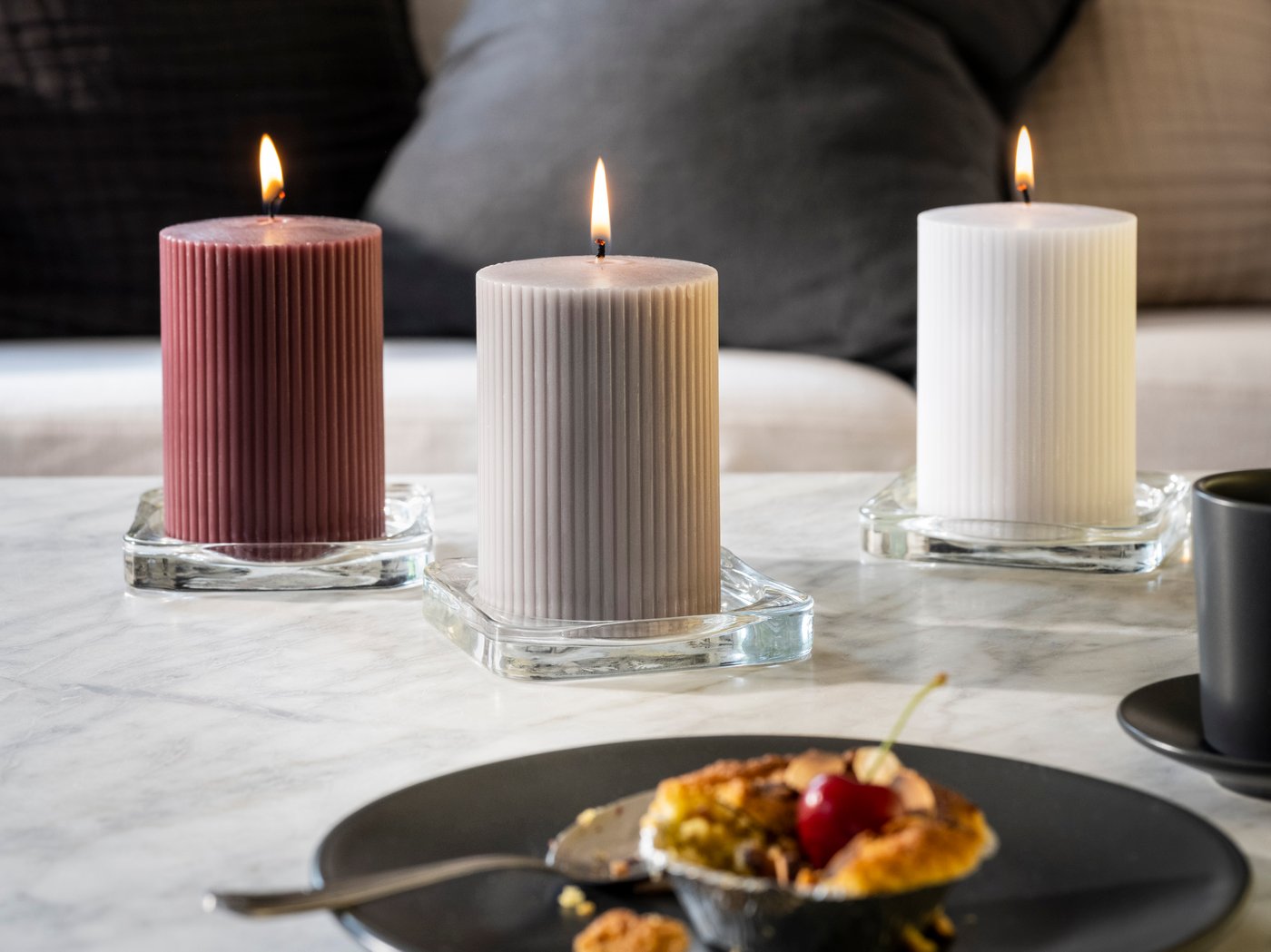 Eetruimte in Scandinavische stijl met brandende KOPPARLÖNN geurkaarsen en theelichtjes op een eettafel bij een groot raam.