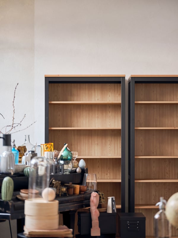 An empty HEMNES cabinet. In front of it stands a table with ceramics, books and storage boxes on its surface.