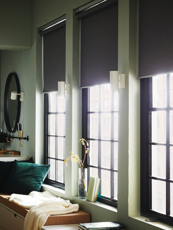 NORDLI drawer units with throws and a cushion on top sit below three windows with half-open FYRTUR block-out roller blinds.