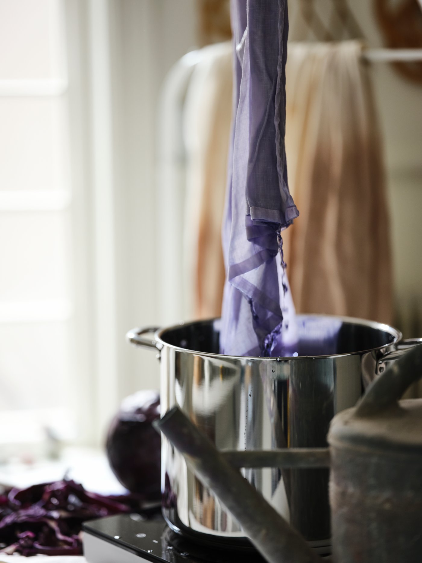 A length of lilac, soaked HANNALILL fabric dripping into an IKEA 365+ stockpot on a white TILLREDA portable induction hob.