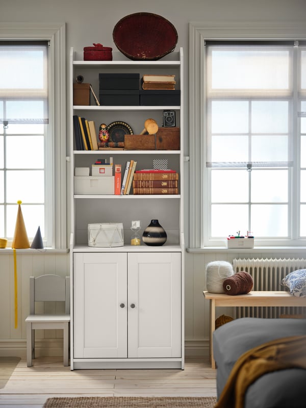 A living-room section where a white HAUGA high two-door cabinet holding storage and decoration stands between two windows.
