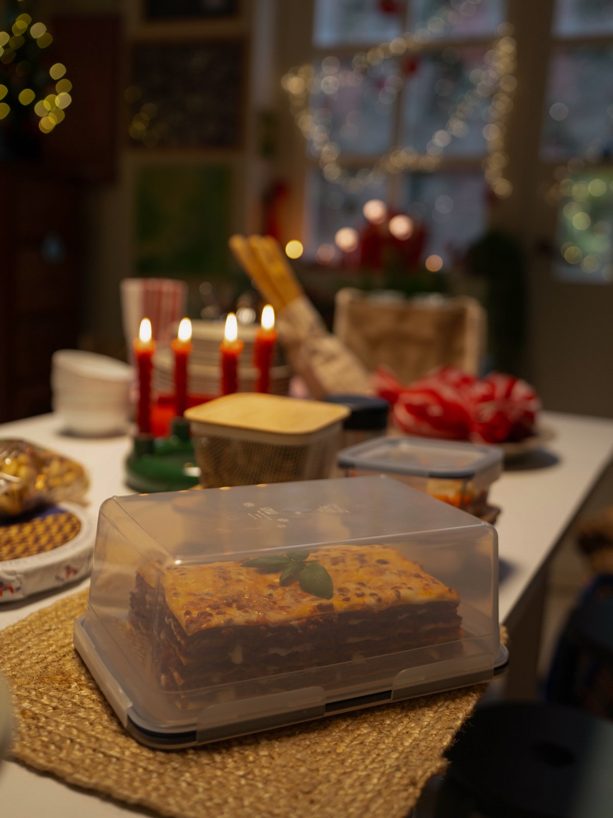 Una lasagna all'interno di un contenitore per alimenti rettangolare IKEA 365+ con coperchio, appoggiato su una tovaglietta in juta.