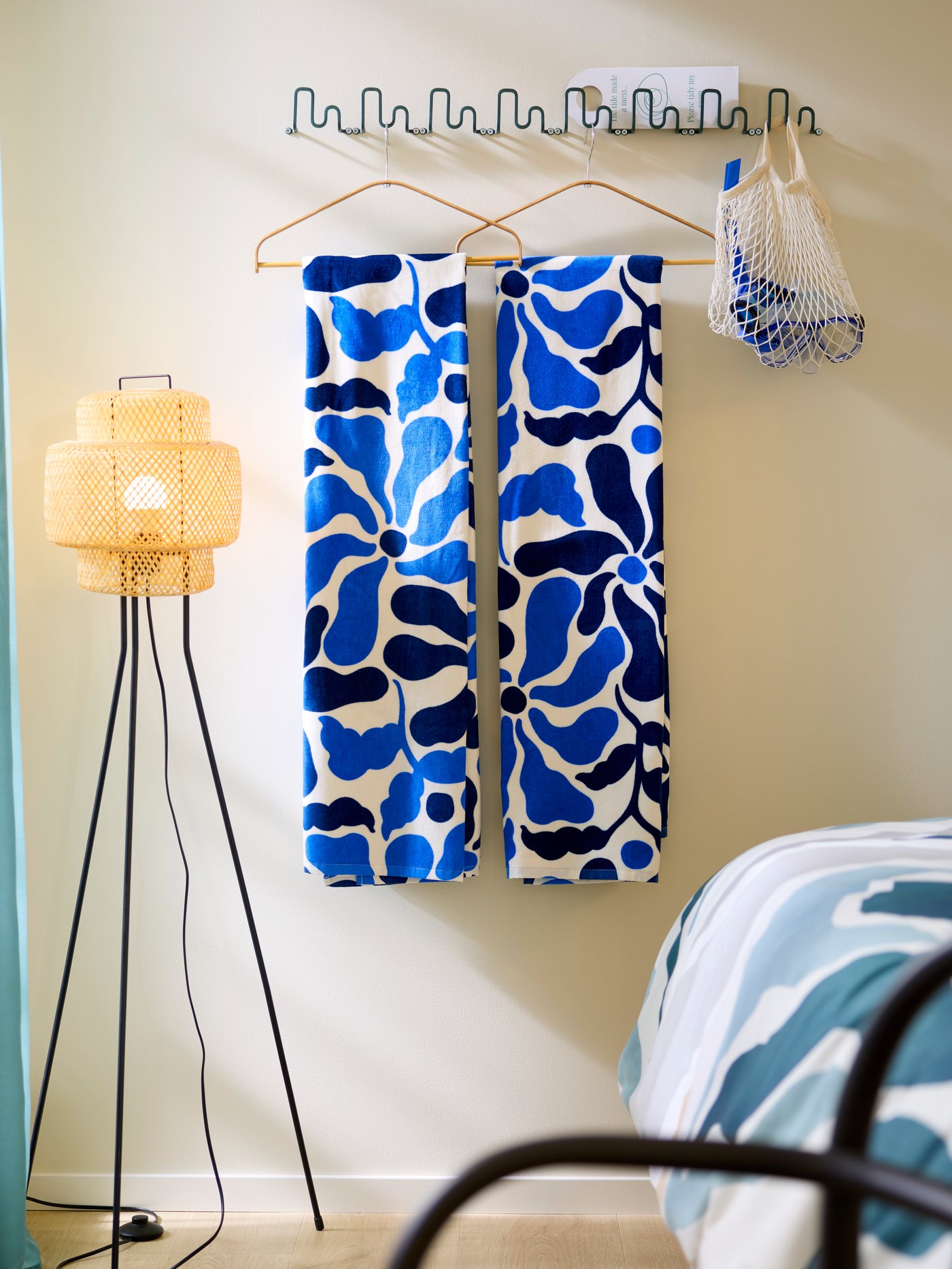 Multiple wave-shaped, dark grey-green JORMÅNEN hooks are on a beige hotel room wall, holding folded beach towels on hangers.