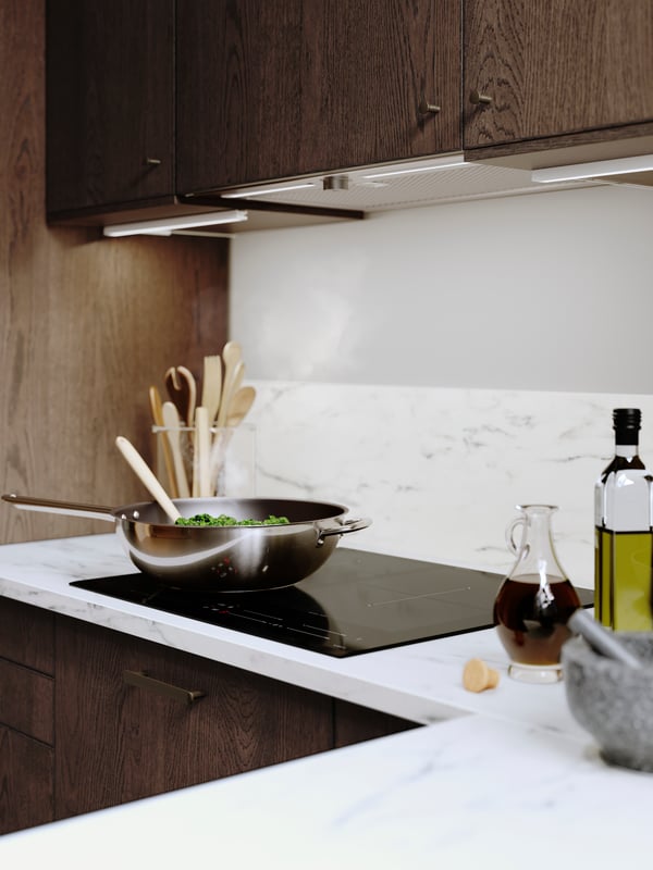 Vista superior de una cubierta laminada EKBACKEN efecto mármol blanco. Se ve la encimera de la cocina con un wok encima y al costado dos frascos de aceite.