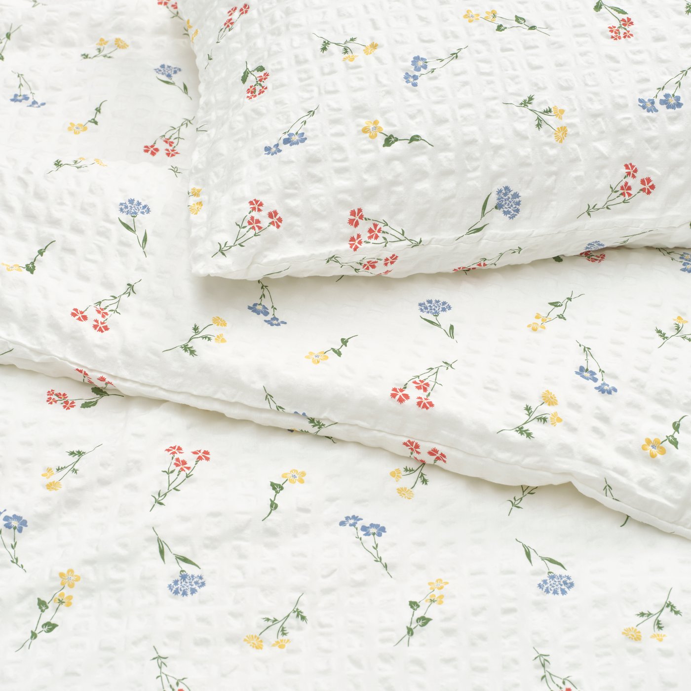 A white/floral pattern PILDVÄRGMAL duvet cover and pillowcase in bed.