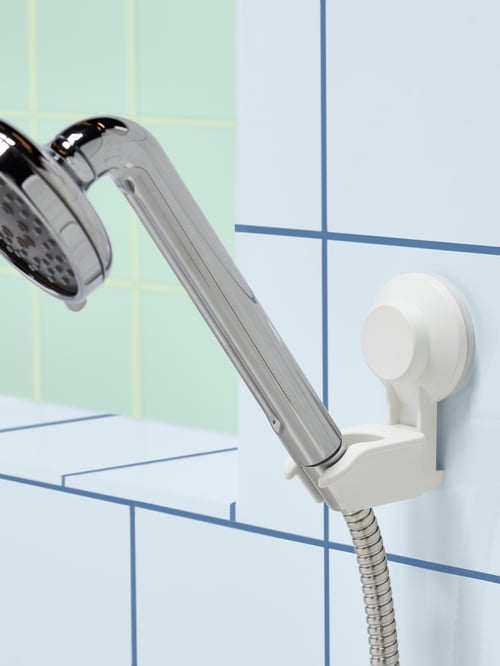 Close-up of white plastic TISKEN hand shower parking bracket with suction cup, holding a hand shower, on a blue tiled wall.