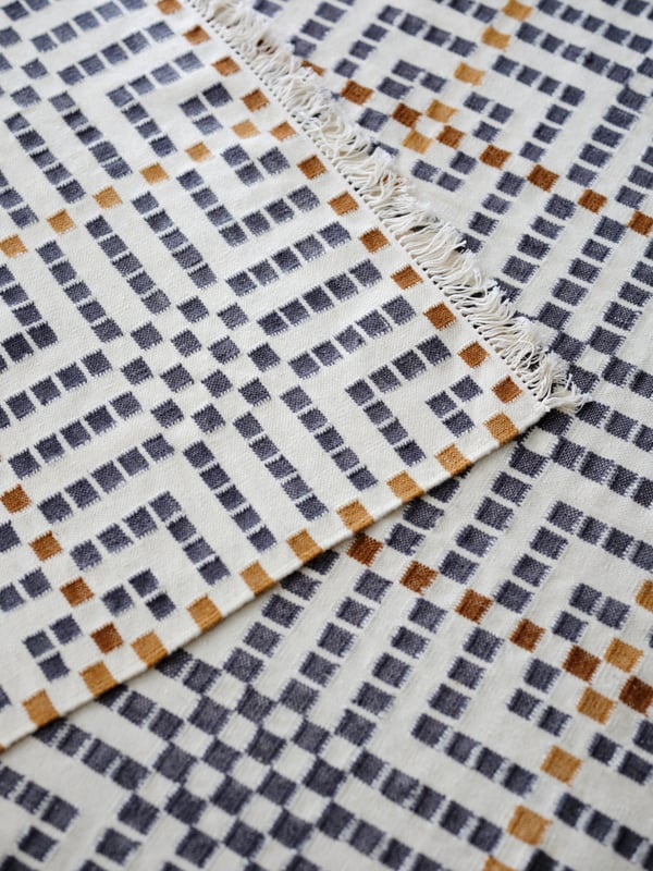 A flatwoven VAMDRUP rug with a multicoloured traditional pattern is layered on top of another VAMDRUP rug.