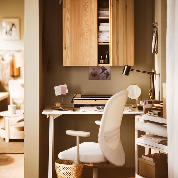 A workspace placed in a corner with dark beige walls, wooden floors, a white TROTTEN desk and a beige FLINTAN office chair.