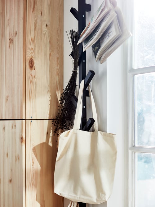 Hallway close-up of a black hanger made of solid wood, supporting a beige carrier bag and other items.