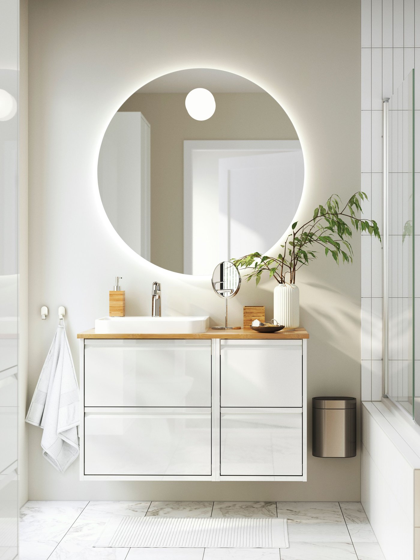 I et hvidt badeværelse hænger et ÄNGSSJÖN vaskemøbel med en lys træbordplade og over den hænger et rundt spejl.