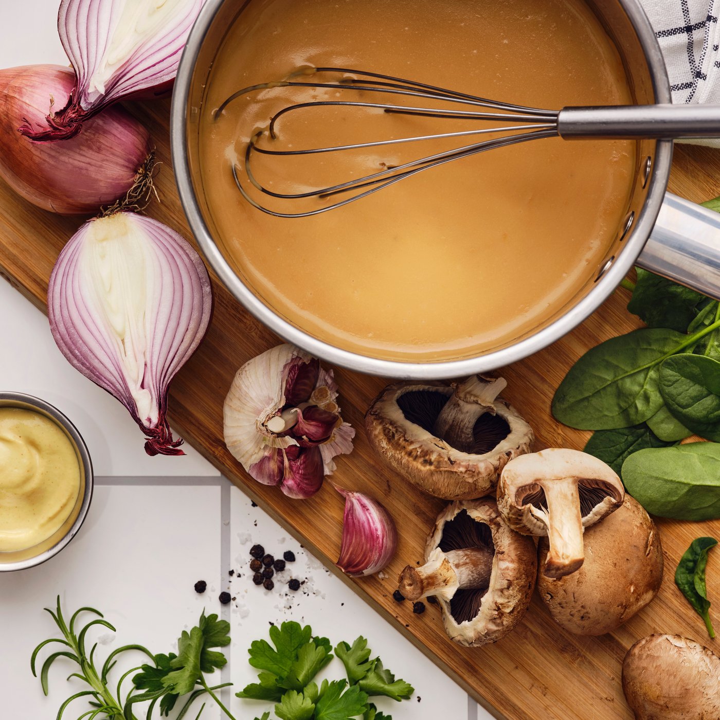 Sobre uma tábua de cortar com alho, cogumelos, folhas de espinafre e chalotas, um batedor numa caçarola com mistura para molho de natas ALLEMANSRÄTTEN.