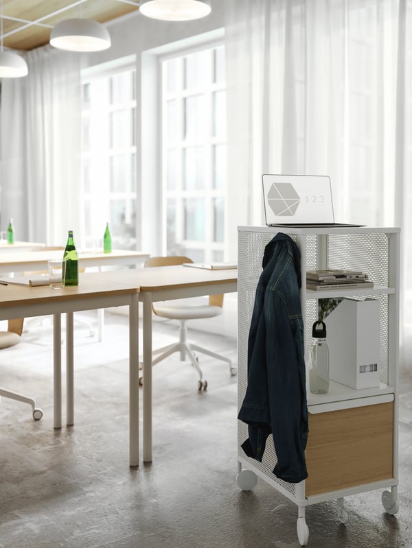 A white storage unit on castors used as a presentation stand in a conference room. A jacket hangs on a hook on its side.