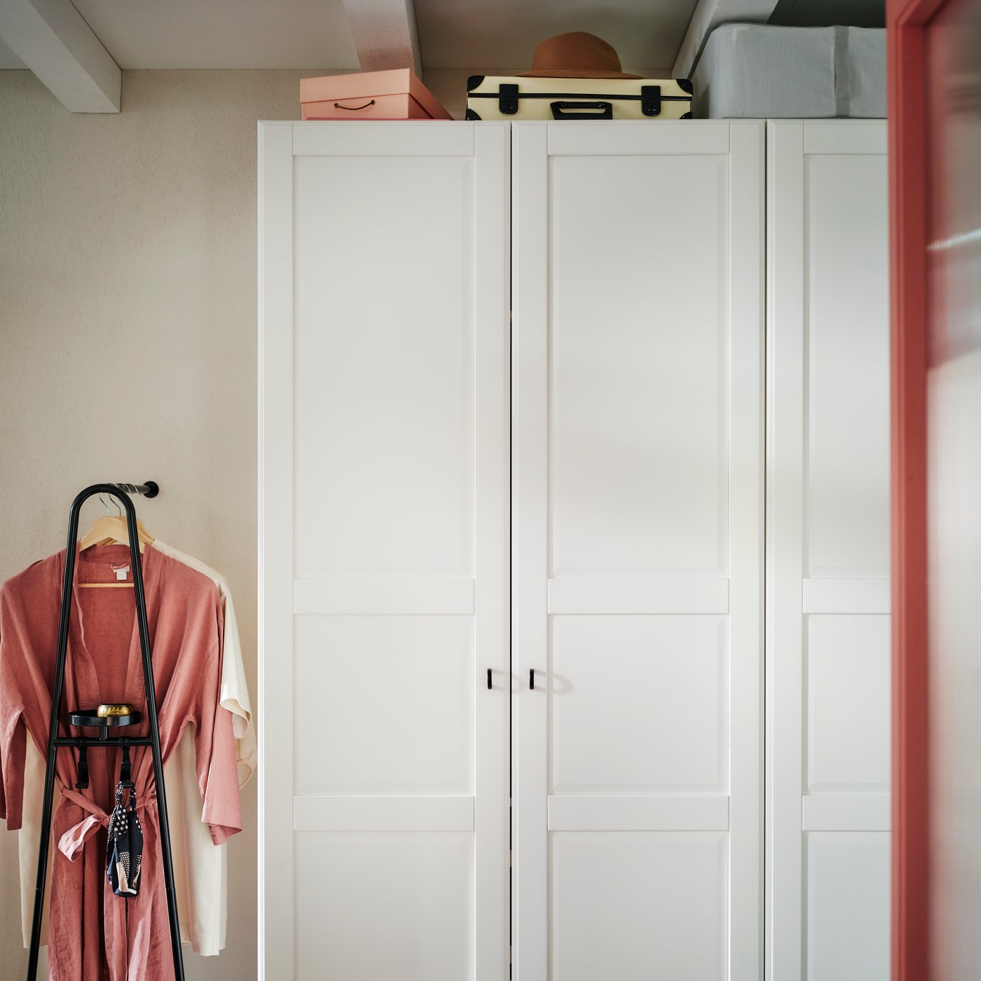 A PAX/TYSSEDAL wardrobe with the doors closed and storage boxes on top and an ÄLGANÄS clothes rack with shoe storage by it it.