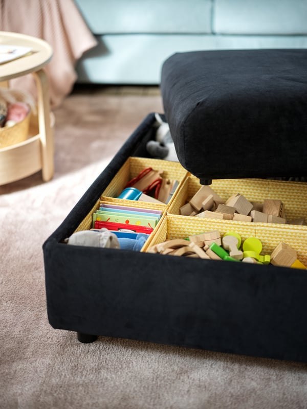 A black-blue VIMLE footstool with its lid half-off, revealing toys sorted in multiple yellow UPPRYMD boxes.