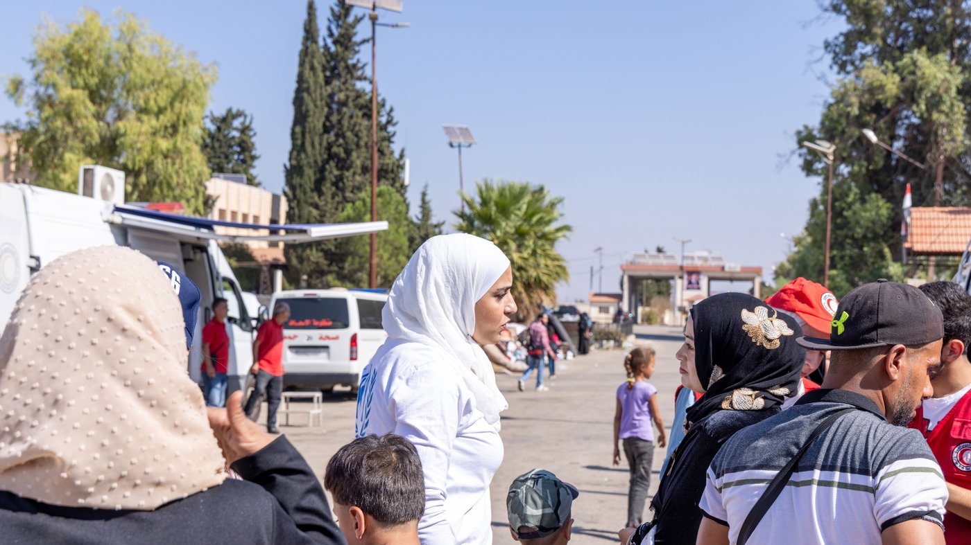 Lujain outside on a street talking to a woman while surrounded by people.
