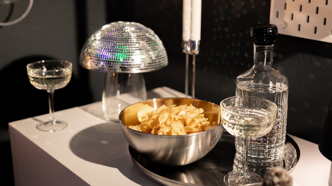 A stainless steel bowl filled with plain crisps sits beside a wine glass and a carafe of clear drink.