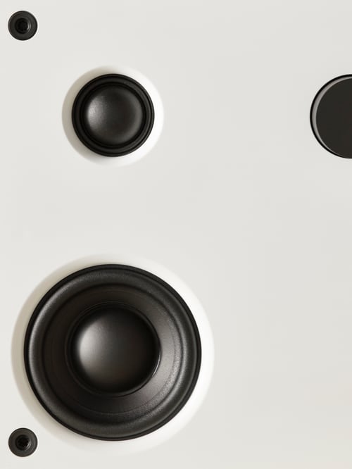 Imagine de prim-plan extremă a părții frontale a unui difuzor Bluetooth VAPPEBY care prezintă difuzoare rotunde, negre, pe o suprafață albă.