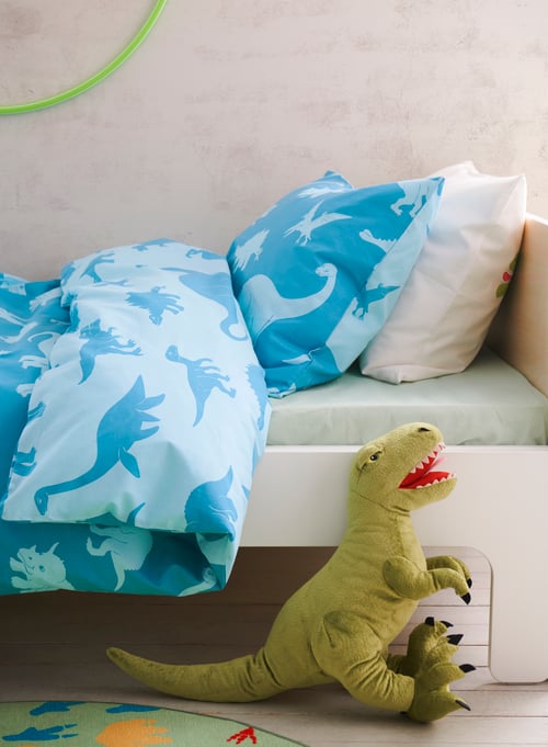 Bedroom with white extendable bed frame, quilt cover and pillowcase with dinosaur pattern, dinosaur shaped soft toy, rug.