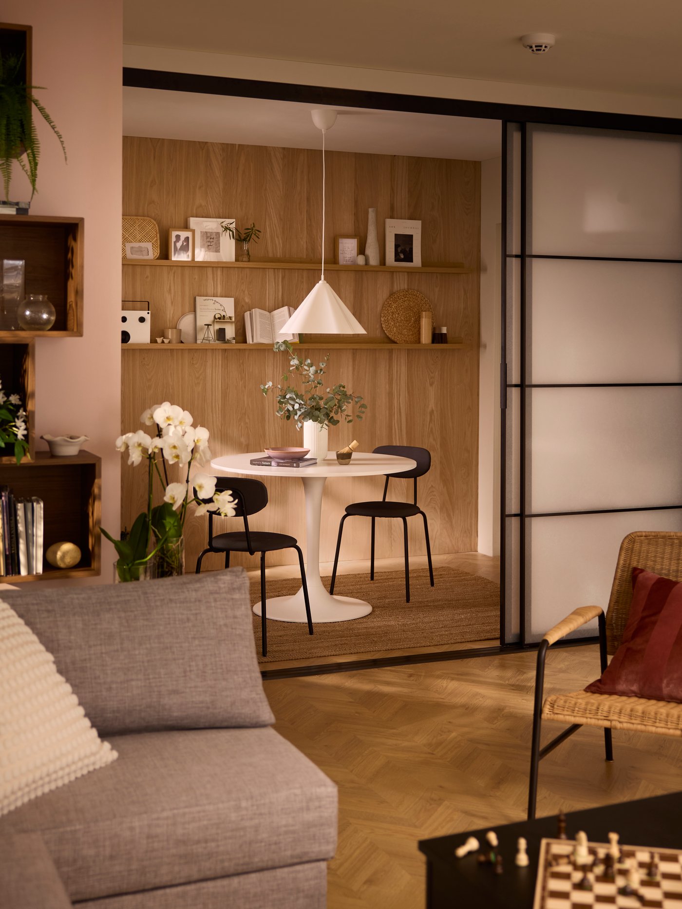 A living room opening up, by way of a pair of SKYTTA sliding doors, onto a dining alcove with a white, round DOCKSTA table.