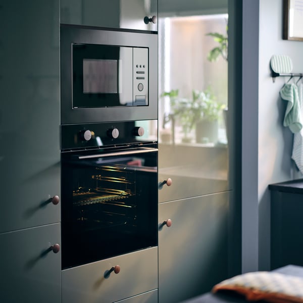 Un four à air pulsé SPJUTBO, situé en dessous d'un four à micro-ondes, intégré dans une cuisine avec des façades KALLARP en gris-vert foncé brillant.