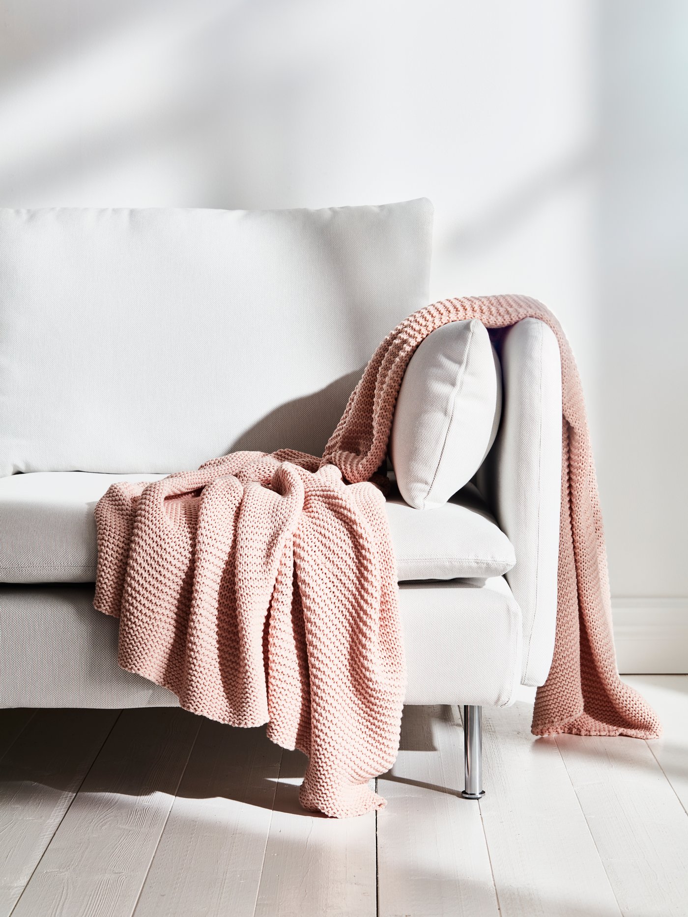INGABRITTA throw on a light coloured sofa on a white wooden floor in front of a white wall.
