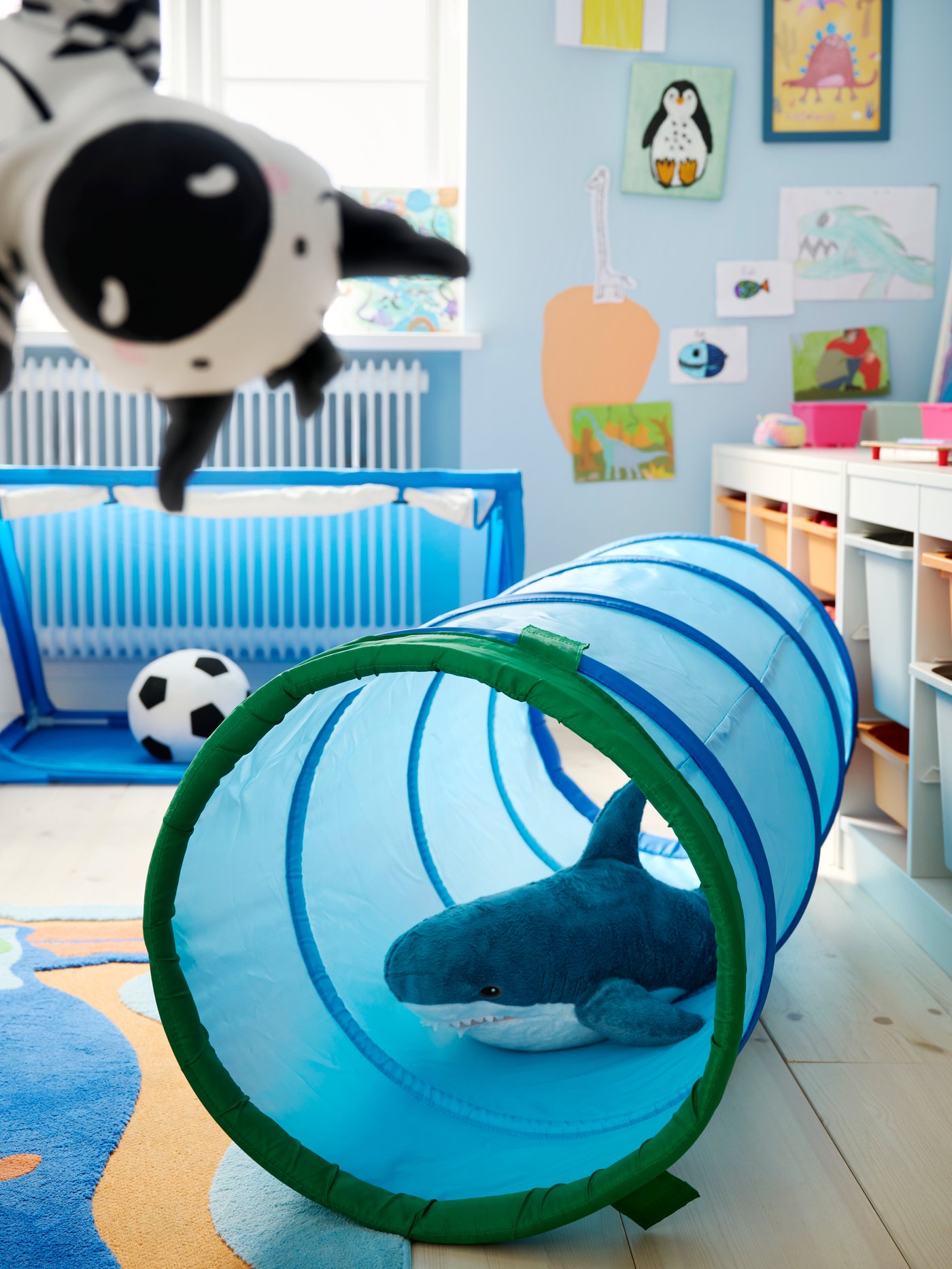 Blue DVÄRGMÅS play tunnel on the floor of a children’s room, with BLÅHAJ soft toy inside it and a hand puppet in foreground.
