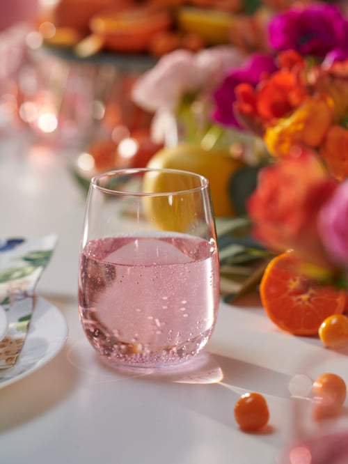 Close-up on table with colourful flowers and classy delicate clear glass made of crystalline holding pink bubbly drink.