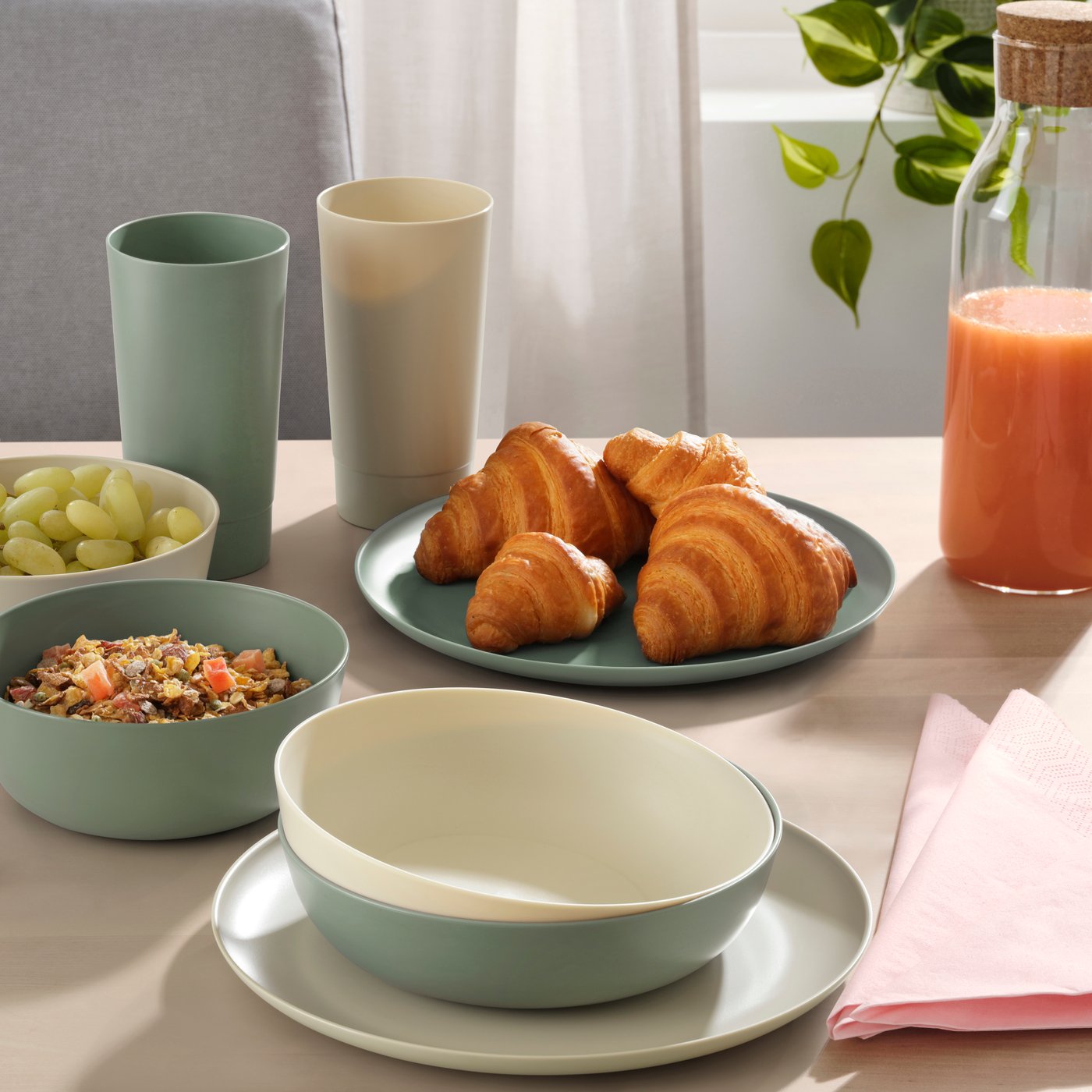 Breakfast table with croissants, bowls, cups, grapes, and a bottle of orange juice.