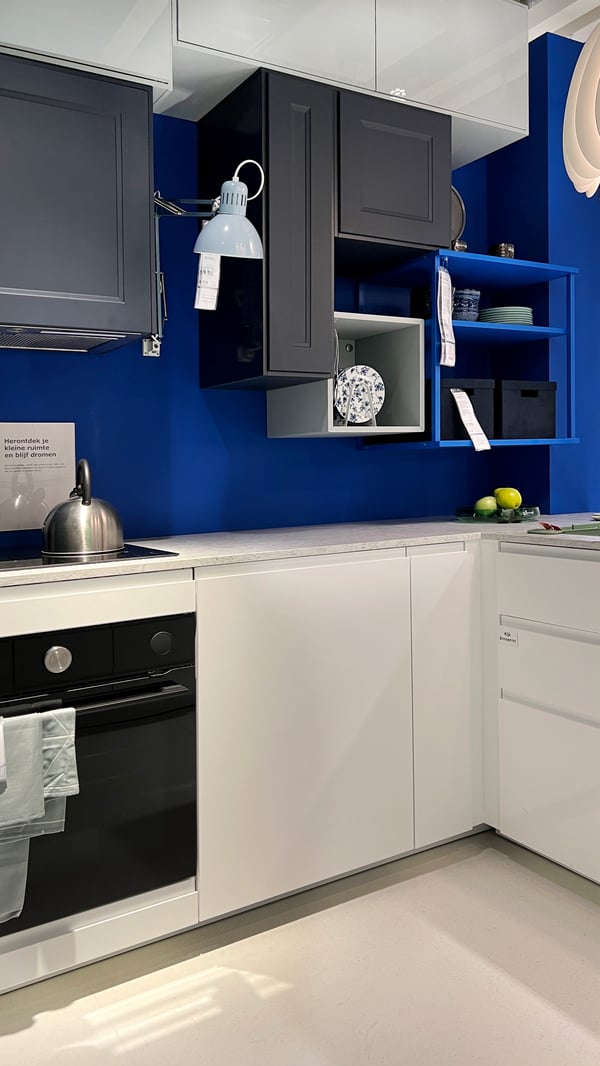 A light, spacious kitchen with a blue back wall and dark blue upper cabinets above a white countertop