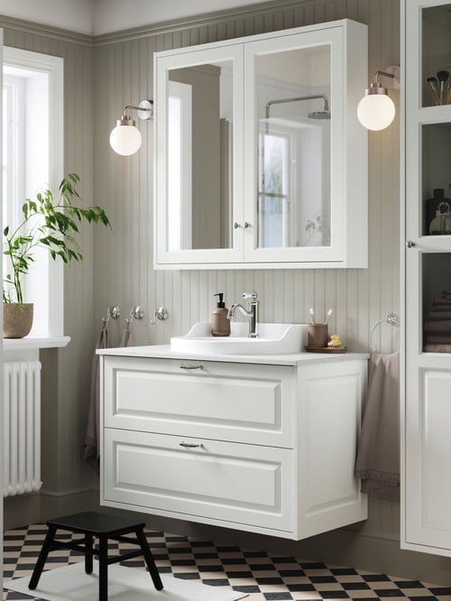 A TÄNNFORSEN wash stand with drawers, a mirror cabinet with doors, and two lit wall lamps, in a checkered floor bathroom.