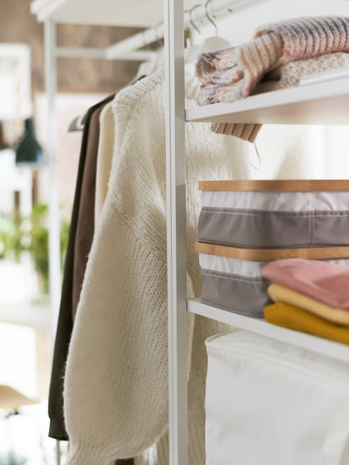 A hanging rail and three shelves on a PLATSA open shelving unit holding clothes and storage boxes in dfferent colours.