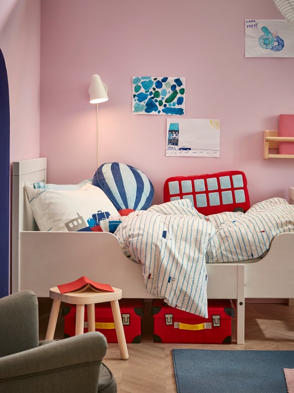 A white SUNDVIK extendable bed with UPPTÅG bed linen and FLYTTBAR trunks for toys underneath stands in a corner.