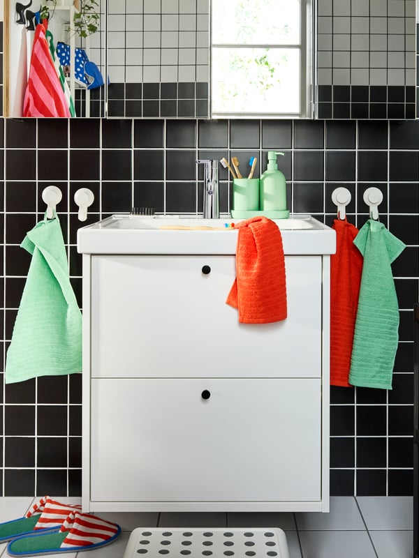 Meuble lavabo HAVBÄCK/ORRSJÖN blanc à deux tiroirs sous quatre armoires à pharmacie. Serviettes multicolores sur crochets blancs.