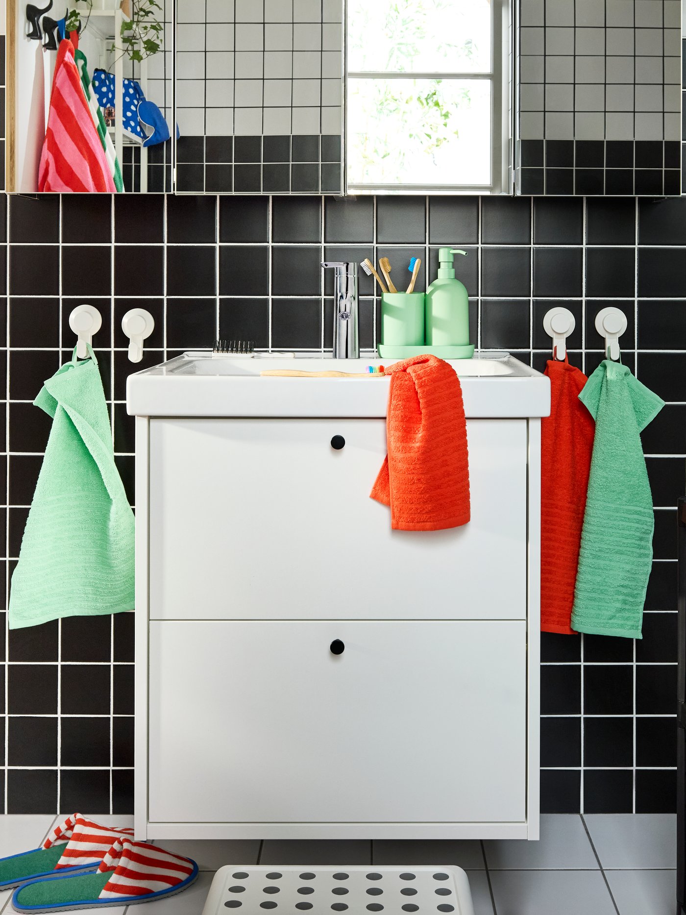 Meuble lavabo HAVBÄCK/ORRSJÖN blanc à deux tiroirs sous quatre armoires à pharmacie. Serviettes multicolores sur crochets blancs.