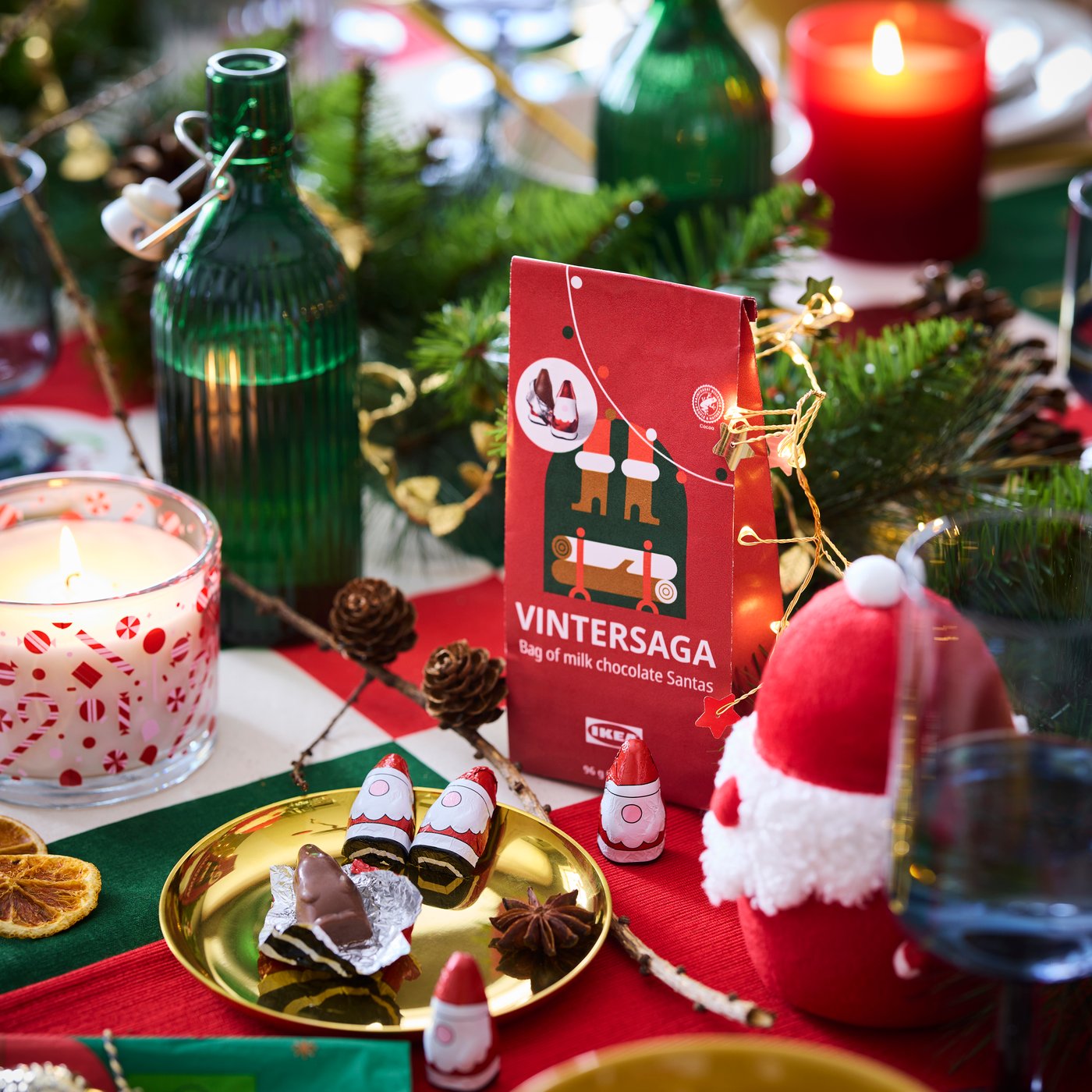 Una confezione di Babbi Natale di cioccolato VINTERSAGA certificata Rainforest Alliance posta su una tavola decorata per le feste con lucine e addobbi.