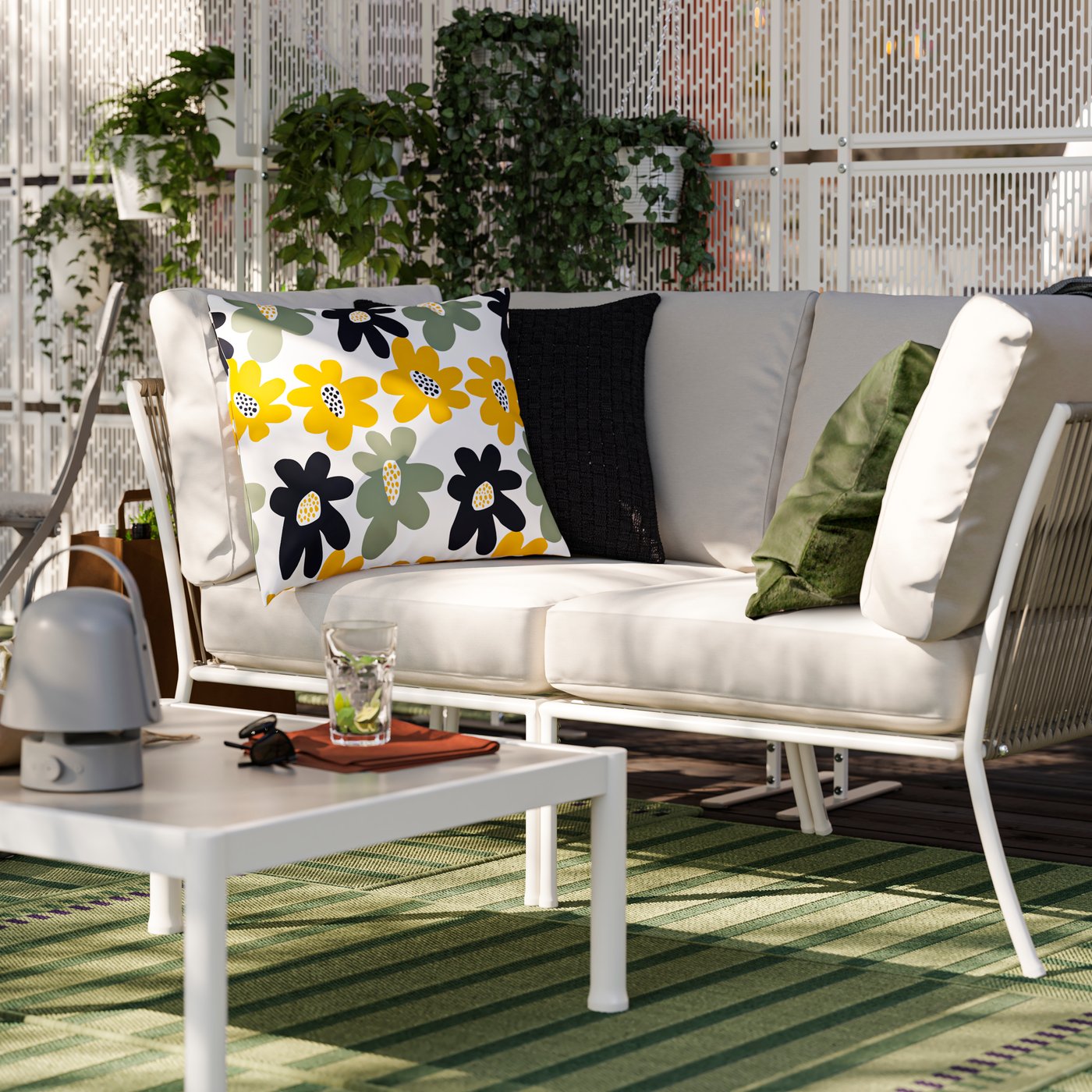 An outdoor lounge area with a SEGERÖN sofa and coffee table. There are green outdoor rugs and privacy screens with plants.