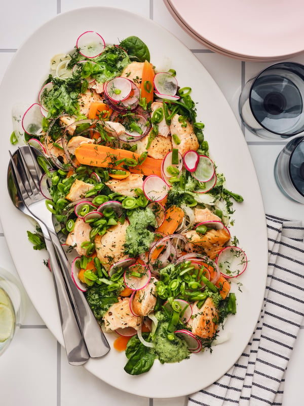 A salad made of pieces of cooked SJÖRAPPORT salmon fillet, carrots, green vegetables and radish is served on a white plate.