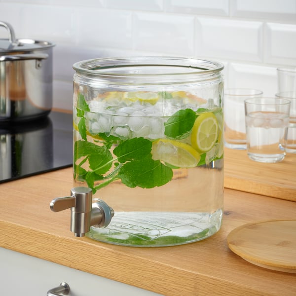 Un dispenser in vetro con rubinetto IKEA 365+ contenente una bevanda sopra un piano di lavoro di una cucina. Il dispenser non ha il coperchio.