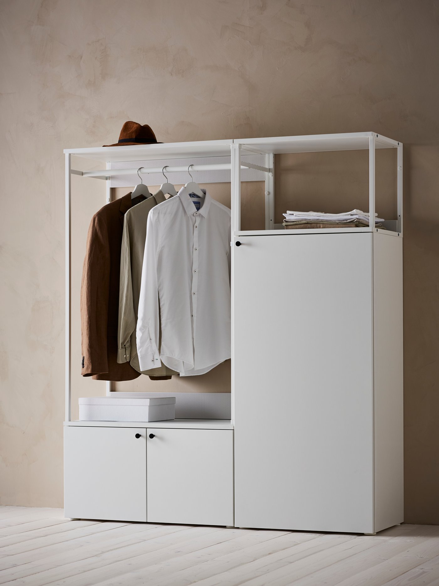 Un armario PLATSA blanco de tres puertas con una caja y documentos en los estantes, un sombrero en la parte superior y camisas colgadas de la barra.