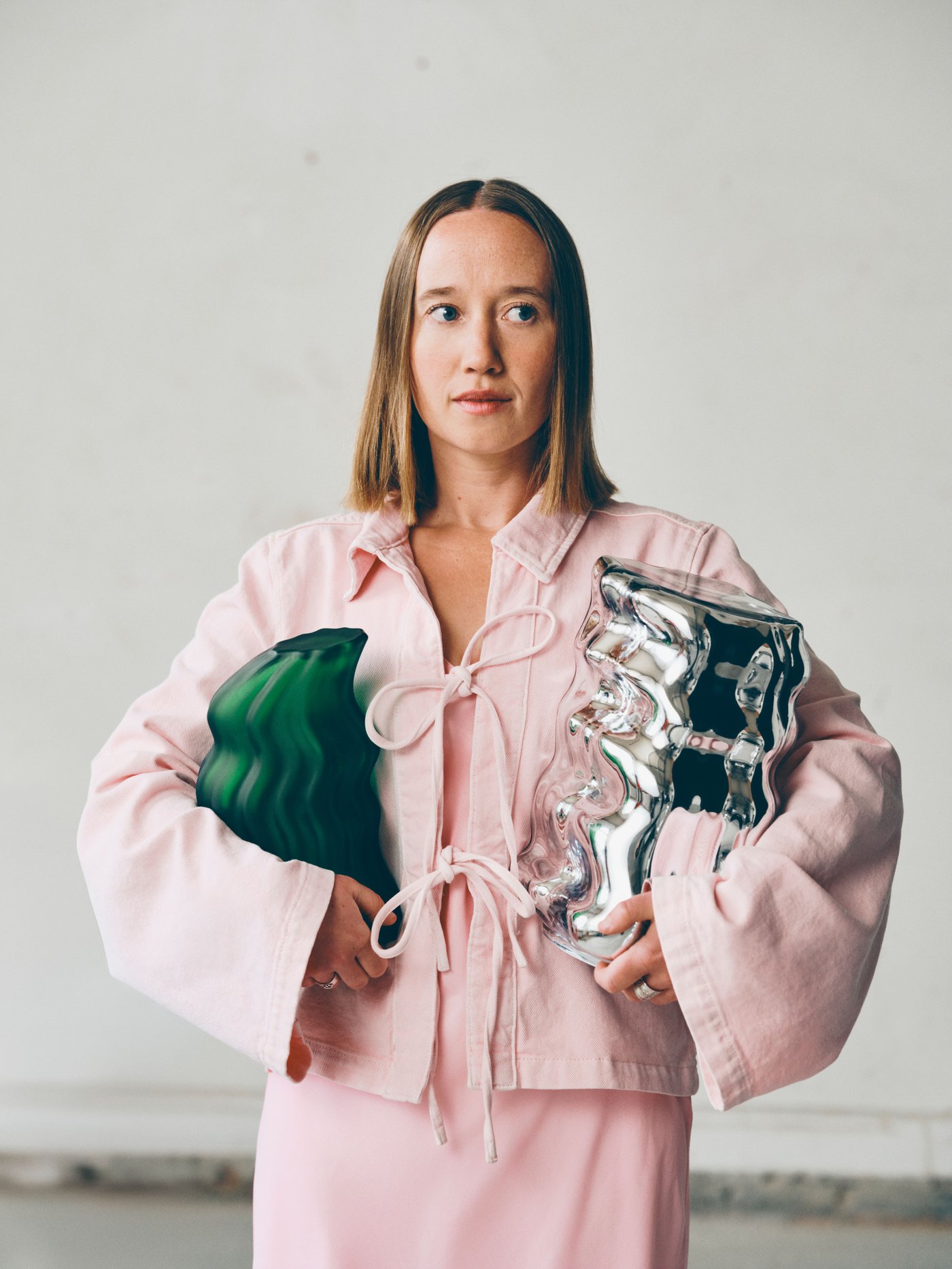 Close up of Lisa Resier in a pink dress holding a green and a metallic sculpture made for IKEA art collection KONSTRUNDA.