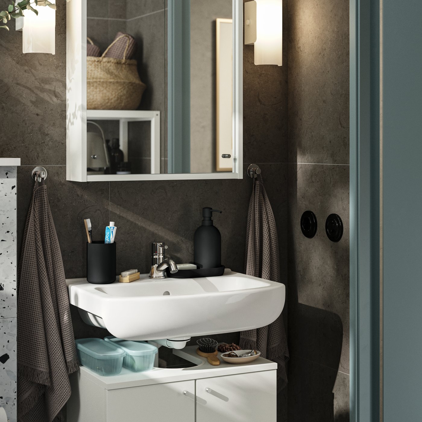 Un piccolo bagno con pareti marrone scuro e mobili bianchi. Un mobile NYSJÖN a due ante offre spazio sotto il lavandino.