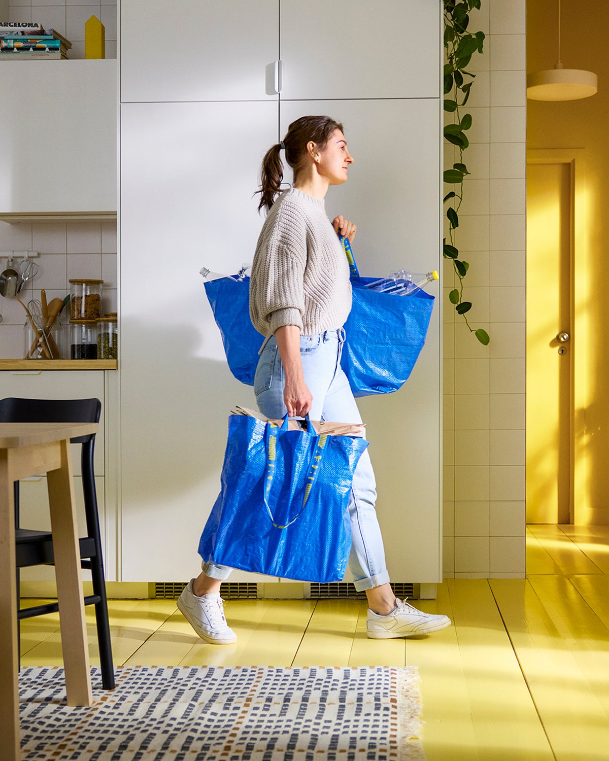 Woman carrying two blue FRAKTA bags at home