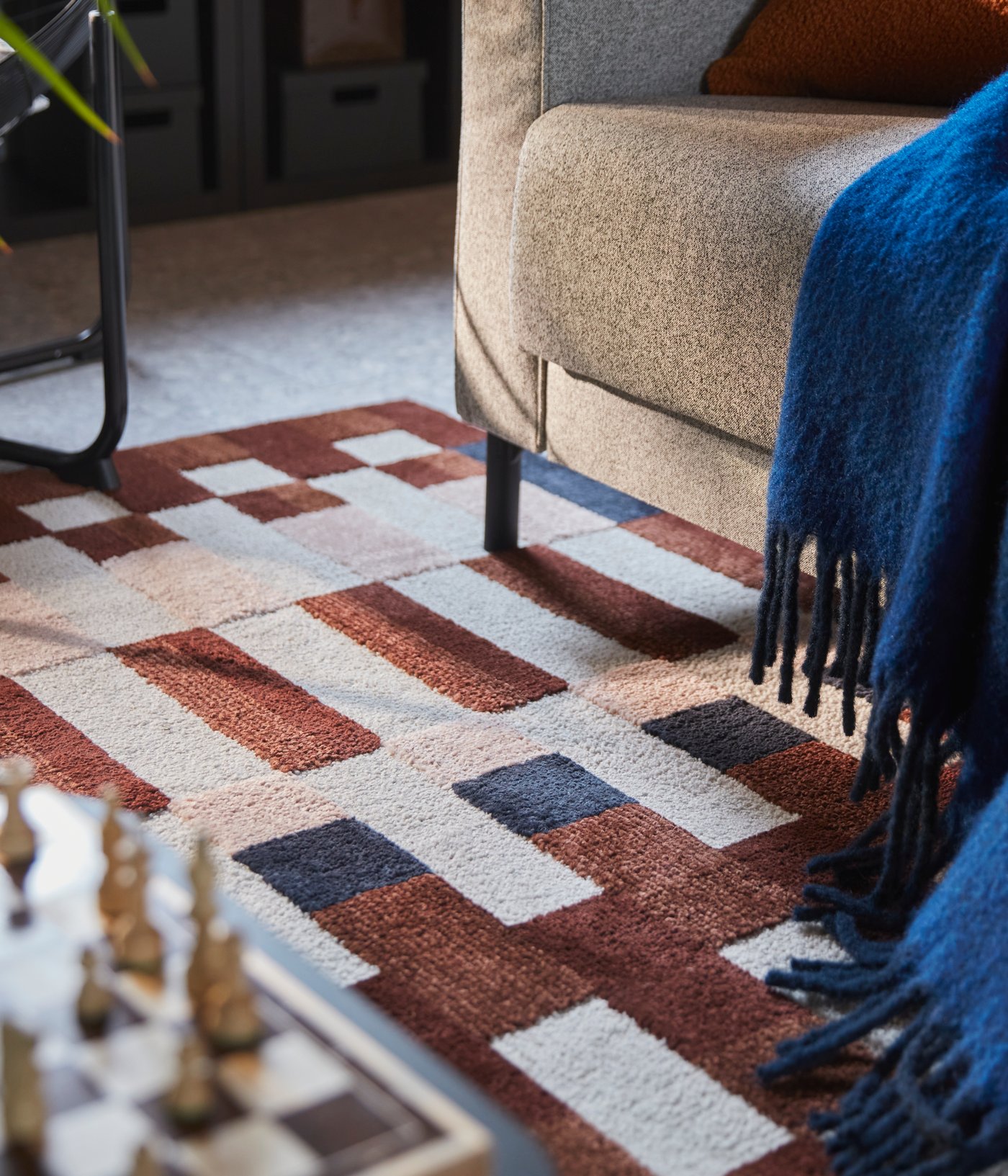 Salon avec tapis à poils ras MARKBLÅMME multicolore avec motif à carreaux sous un canapé et à côté d’un jeu d’échecs.