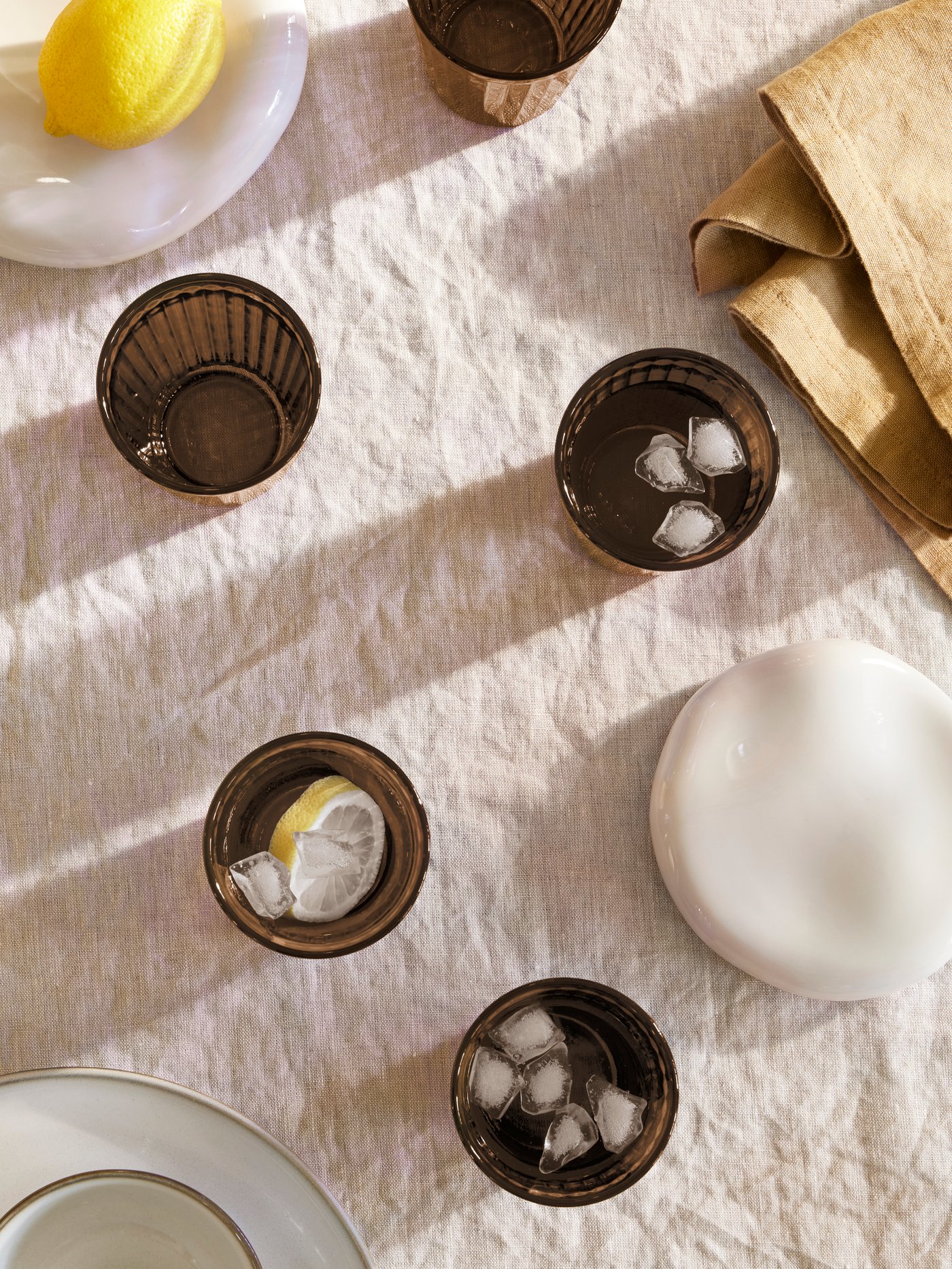 An OMBONAD tablecloth with VARDAGEN glasses in brown holding drinks with ice cubes and a GLADELIG plate in grey with a cup.