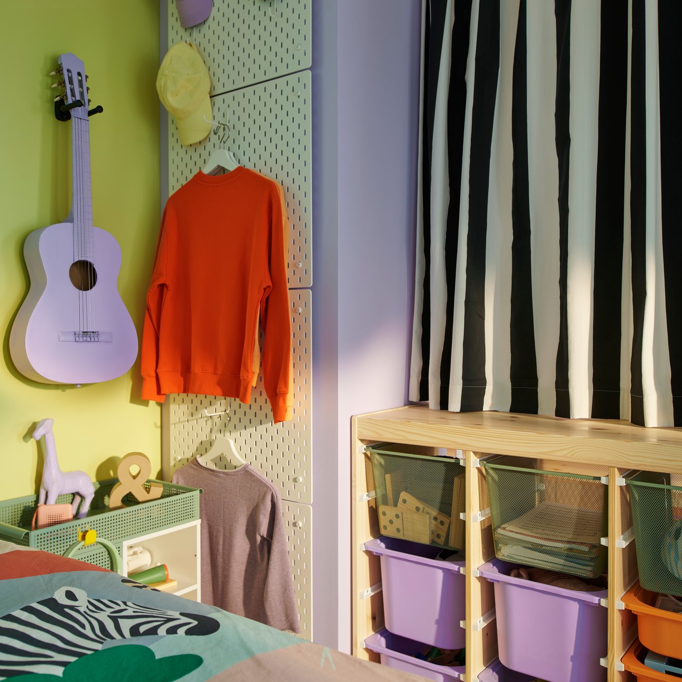 TROFAST paravan iznad kog je navučena zavesa s crno-belim prugama nalazi se pored četiri bele vertikalno postavljene SKÅDIS perforirane ploče.