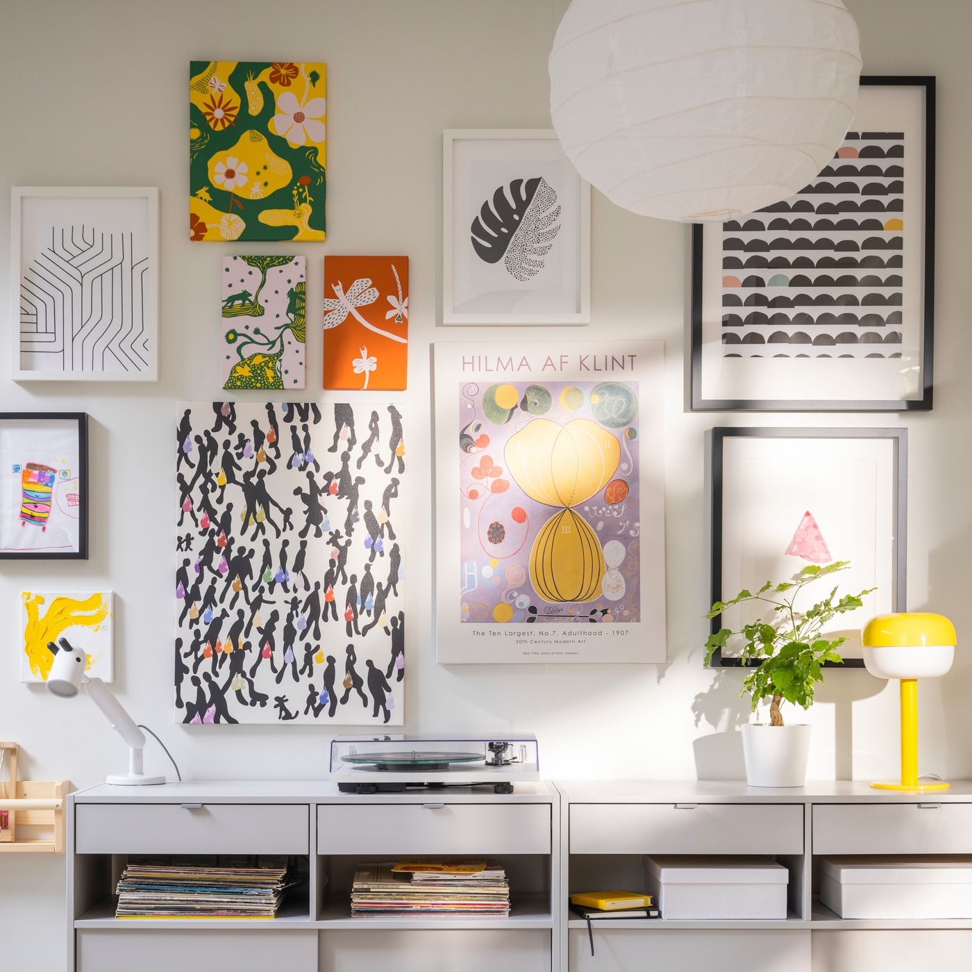 IKEA SPIKSMED light grey sideboards, one with a record player on top, stand against a wall where many pictures are hanging.