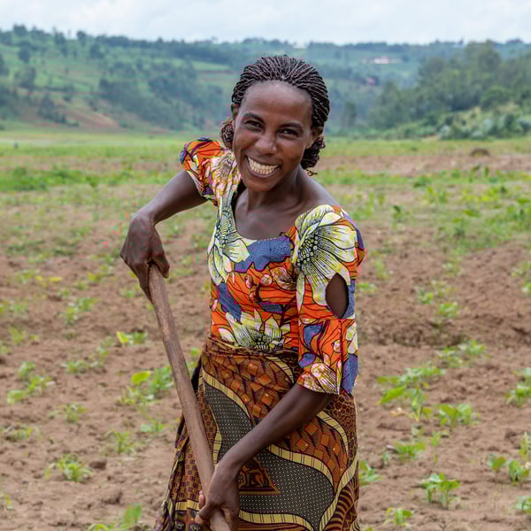 A woman looking in the camera smiling and working the soil with a rake