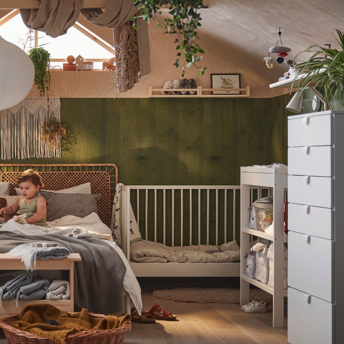 Eine erwachsene Person sitzt mit einem Kind auf einem Doppelbett mit neutralfarbenen Textilien. Daneben steht ein GULLIVER Babybett.