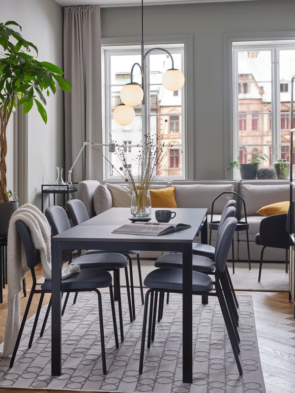 An IKEA VANGSTA dining table in black brown with grey dining chairs, in a bright dining room with white floors and a grey rug.